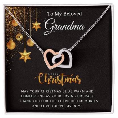 A Christmas-themed necklace featuring two interlocking heart pendants, one in silver and one in gold color, with cubic zirconia crystals, packaged in a box with 'To My Beloved Grandma - Cherished Memories' text and decorative gold stars.
