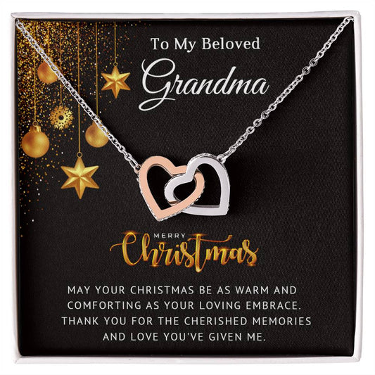 A Christmas-themed necklace featuring two interlocking heart pendants, one in silver and one in gold color, with cubic zirconia crystals, packaged in a box with 'To My Beloved Grandma - Cherished Memories' text and decorative gold stars.